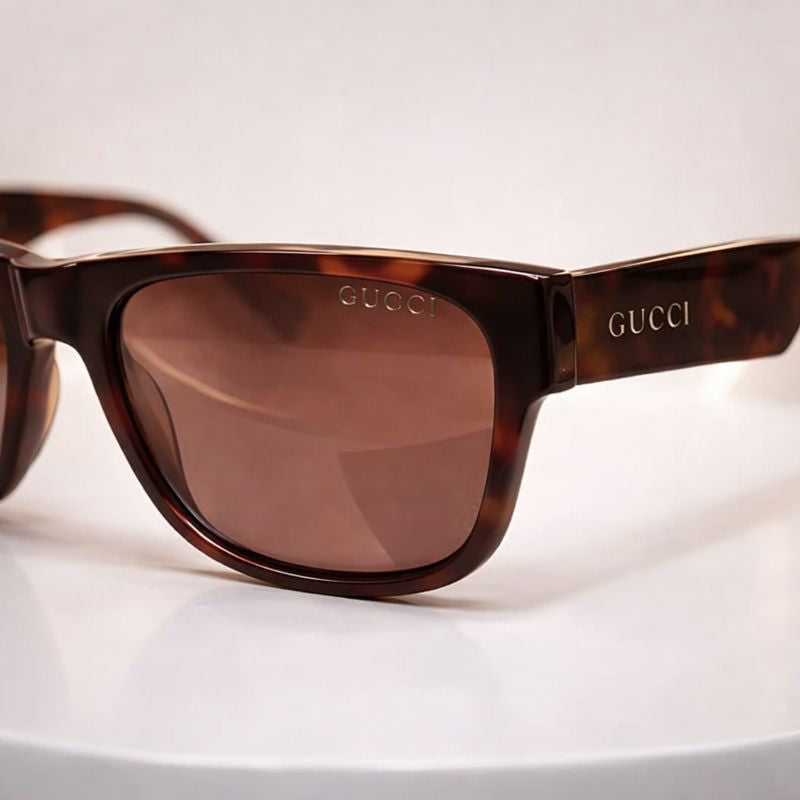Close-up detail of Gucci tortoise shell sunglasses showing gold logo on lens and temple.